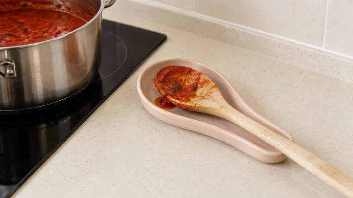 Cuchara con restos de salsa sobre un plato junto a una olla